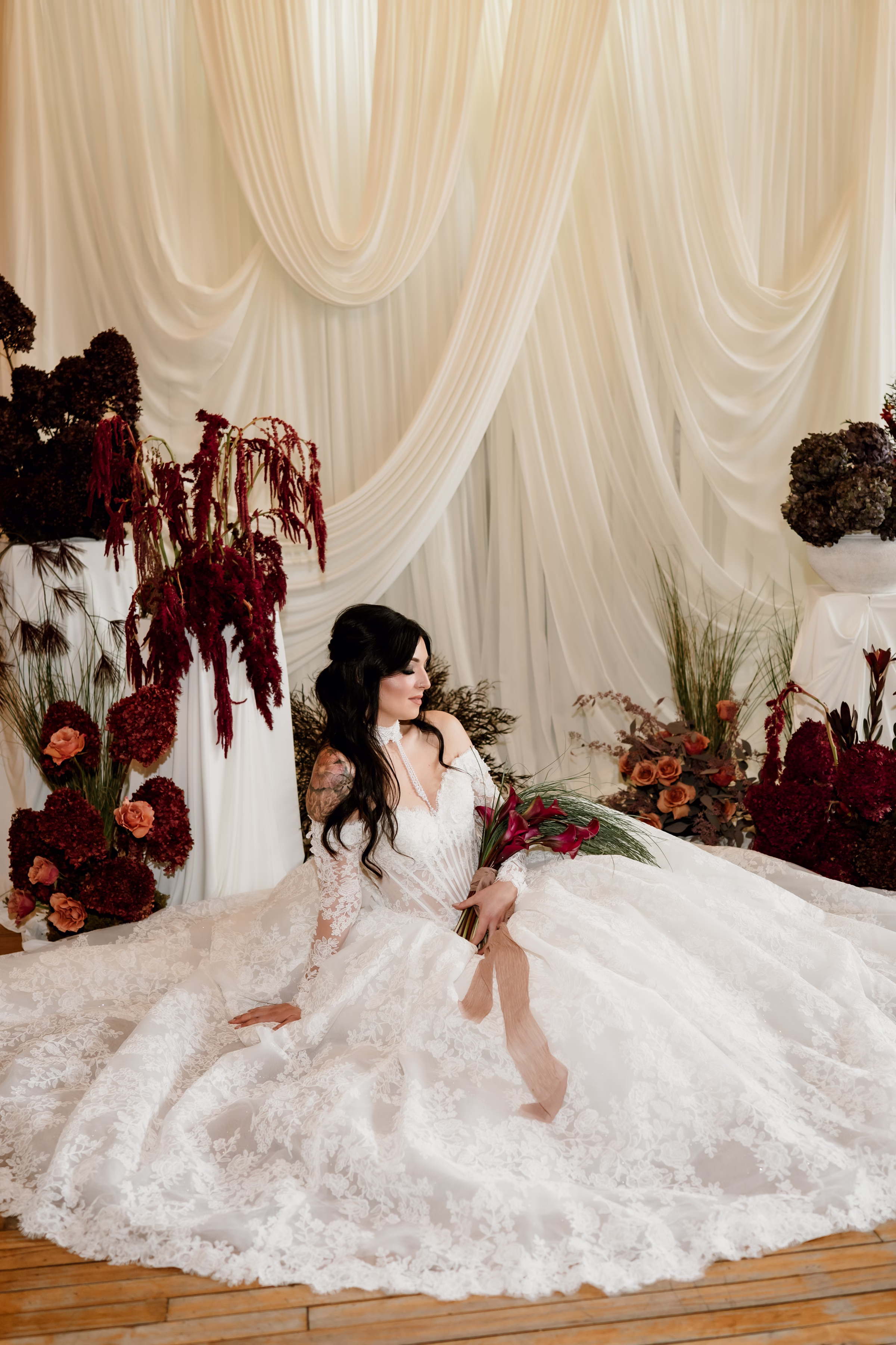 rich velvet fall wedding inspiration mercantile hall burlington wisconsin ceremony draping bride fashion 137 - Rich Velvet Fall Wedding Inspiration at Mercantile Hall in Burlington, Wisconsin a bride model sits at a wedding ceremony surrounded by fall florals and foliage and holding a bridal bouquet of deep burgundy calla lilies with cascading bear grass