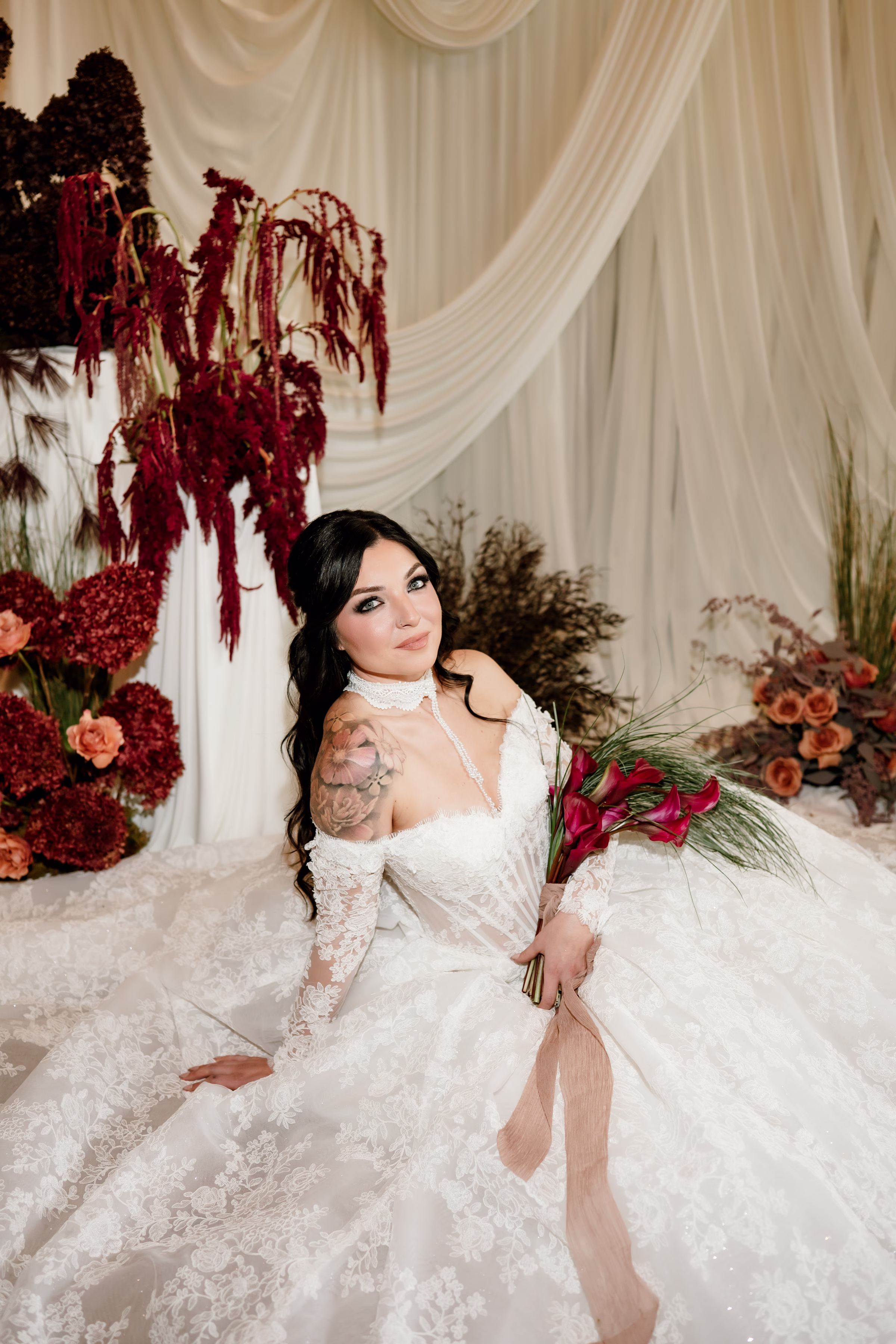 rich velvet fall wedding inspiration mercantile hall burlington wisconsin ceremony draping bride fashion 144 - Rich Velvet Fall Wedding Inspiration at Mercantile Hall in Burlington, Wisconsin a bride sits in front of a wedding ceremony backdrop from Dream House Events, LLC. She is wearing a lace dress from Bon Bon Belle Bridal Boutique and posing in front of green and burgundy fall florals